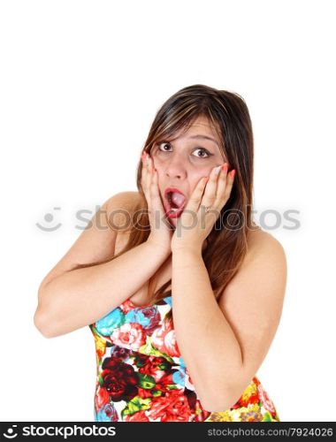 A scared young woman in a colourful short summer dress standing in profileholding her hands on her face, isolated for white background.