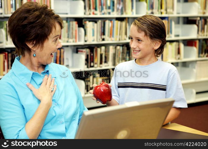 A school boy surprising his teacher with an apple.