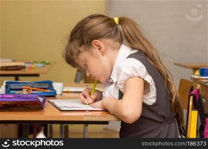 A schoolgirl in a lesson crouched writes in a notebook
