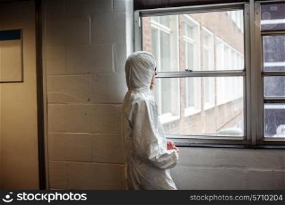 A scientist wearing a boiler suit is standing by a window