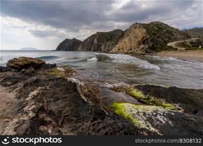 A secluded sandy beach on a wild mountainous coastline with colorful rocks and algae in the foreground