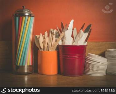 A selection of cutlery, colorful straws and plastic lids for disposable cups on a wooden table