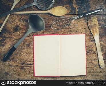 A selection of kitchen utensils on a wooden table with an open book