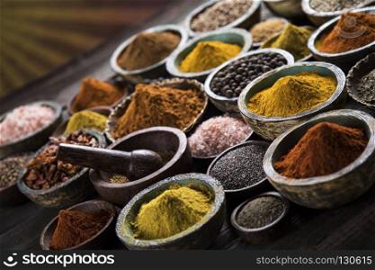 A selection of various colorful spices on a wooden table in bowl. Variety of spices and herbs on kitchen table