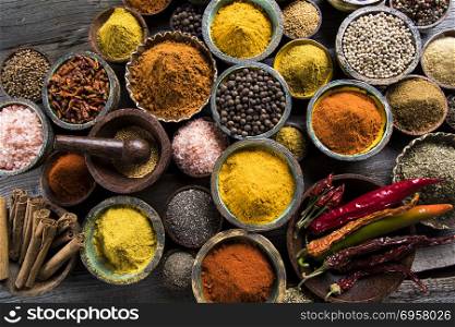A selection of various colorful spices on a wooden table in bowl. Variety of spices and herbs on kitchen table