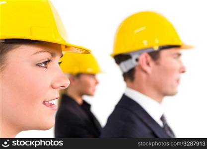 A selective focus industrial concept shot showing 2 women and a man dressed in hard hats. The focus is on the woman in the foreground