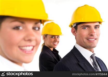 A selective focus industrial concept shot showing 2 women and a man dressed in hard hats. The focus is on the man on the right of the shot.