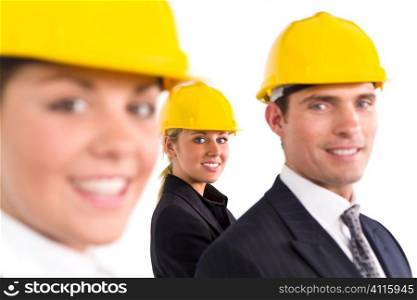 A selective focus industrial concept shot showing two women and a man dressed in hard hats. The focus is on the woman in the background