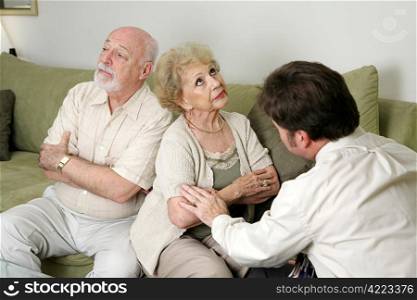 A senior couple in marriage counseling. They have their backs turned and are ignoring eachother while the therapist tries to reconcile them.