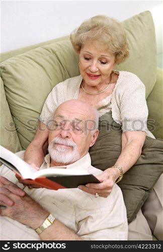 A senior couple reading together. The wife is reading to the husband.