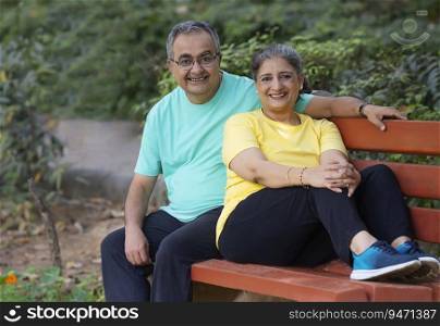 A SENIOR COUPLE SITTING TOGETHER IN A PARK AND LOOKING AT CAMERA