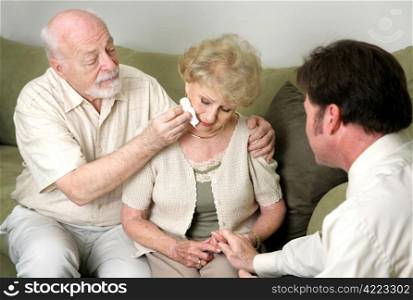 A senior couple with a counselor or funeral director. She is crying and they are comforting her.