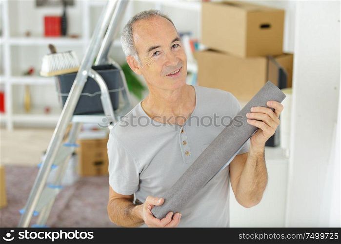 a senior handyman holding wallpaper
