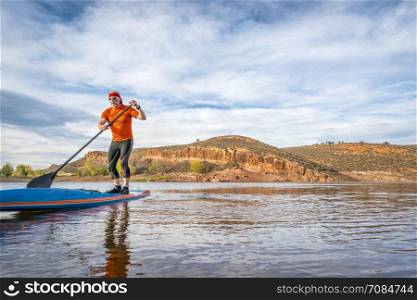 A senior male paddling on a stand up paddleboard on a calm mountain lake - Horsetooth Reservoir near Fort Collins, Colorado, fall scenery