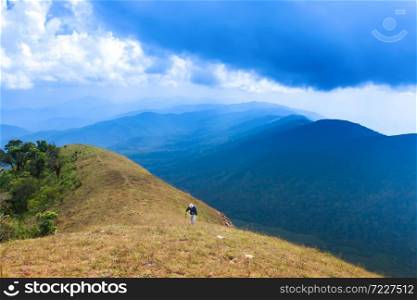 A senior man hiking with hiking pole on the peak of mountain, magical blue clouds and mountain range in the backgrounds.