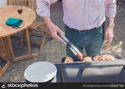 A senior man is attending to a barbecue in the garden on a sunny day