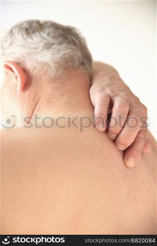 A senior man tries to reach a spot in the middle of his back.