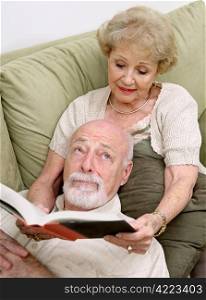 A senior woman reading to her husband who is rolling his eyes in boredom.