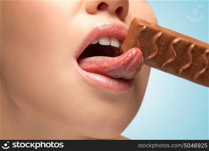 A sensual young woman with tasty lips licking a chocolate bar.