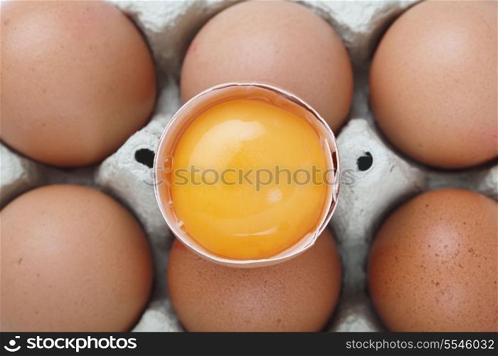 A separated yolk, still in the shell, on top of a carton of brown free-range eggs