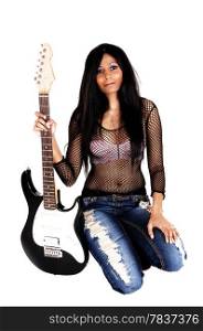 A serious looking Hispanic woman kneeling isolated for white background holding her guitar, in ripped jeans and smiling.