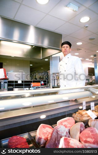 A serious satisfied butcher behind a fresh meat counter in a deli