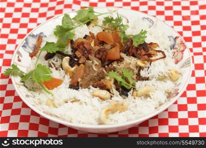 A serving bowl of home-made biryani-type fragrant lamb curry, cooked with dried apricots and yoghurt and garnished with toasted cashews, fried onions and coriander, served with cardamom-flavoured basmati rice.