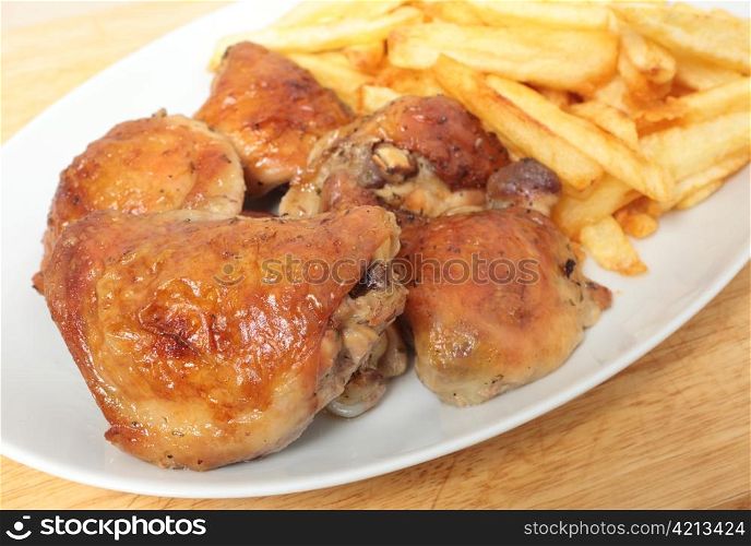 A serving dish piled with roast lemon chicken thighs and French fries, or chips, with a serving spoon