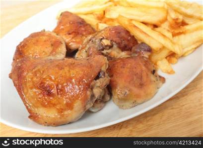 A serving dish piled with roast lemon chicken thighs and French fries, or chips, with a serving spoon