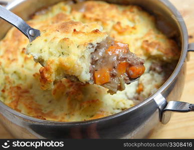 A serving spoon full of shepherd&acute;s pie (minced meat and vegetable stew topped with mashed potatoes baked to a golden crust) over the cooking pot.