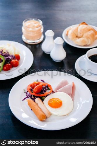 A set of American breakfast sunny side up eggs, sausage, ham, fresh salad bell peppers, tomato, croissant bread with black coffee