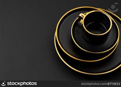 A set of black and golden ceramic plates and cup on a black background. Set of black and golden ceramic plates and cup on a black background