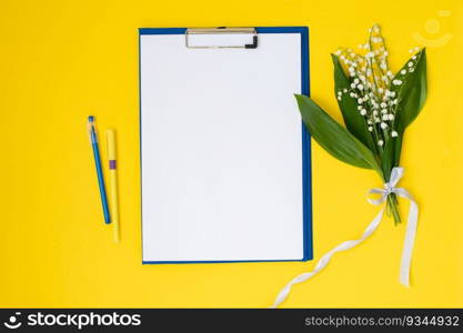 A set of blue stationery as a template with a place to copy on a yellow table with lilies of the valley flowers, a tablet, a pen, a pencil, a folder for papers. Top view, recording location. A blue folder a template with a place to copy on a yellow table with lilies of the valley and pens