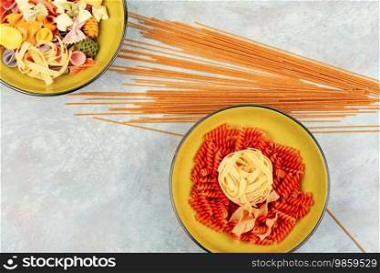 A set of dry colorful macaroni, uncooked pasta and spaghetti. Space for text.. Bowl with raw pasta on cooking table