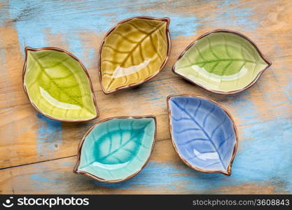 a set of empty, leaf shaped, ceramic side dish bowls against grunge painted wood