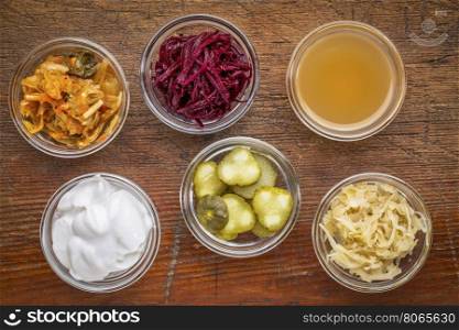 a set of fermented food great for gut health - top view of glass bowls against wood: kimchi, red beets, apple cider vinegar, coconut milk yogurt, cucumber pickles, sauerkraut