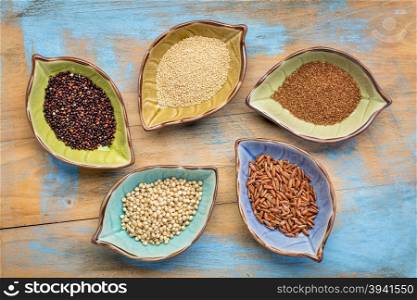 a set of five gluten free grains (sorghum, teff, amaranth,brown rice and quinoa) - top view of leaf shape bowl against grunge, painted wood