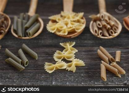 A set of raw pastas on spoons on a wooden table. A set of raw pasta on a wooden table. Studio Shot