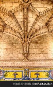 A set of stone beams spread out from a single column over a row of decorative tiles to support the ribbed vaulted ceiling of a portion fo the Jeronimos Monastery in Belem, Portugal.