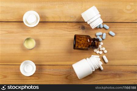 A set of three different bottles of pills and a variety of pills. Against a wooden background.. A set of three different bottles of pills and a variety of colour pills.
