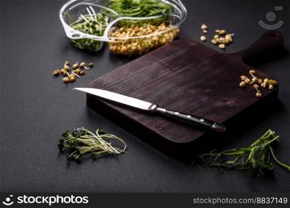 A set or mix of pea, mustard and sprouted mung bean microgreens in a portioned plastic box on a dark concrete background