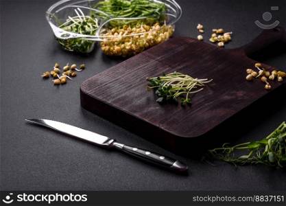 A set or mix of pea, mustard and sprouted mung bean microgreens in a portioned plastic box on a dark concrete background