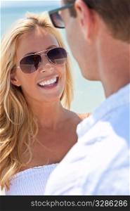 A sexy and attractive man and woman couple wearing sunglasses and having romantic fun laughing in the sunshine at the beach