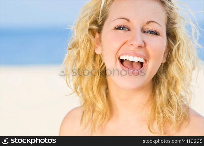 A sexy and beautiful young blond woman gives a big natural laugh whie at the beach