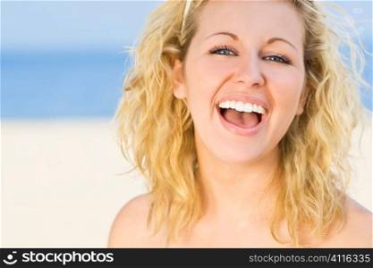 A sexy and beautiful young blond woman gives a big natural laugh whie at the beach