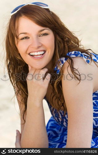 A sexy and beautiful young brunette woman sitting at the beach happily laughing with golden sand behind her