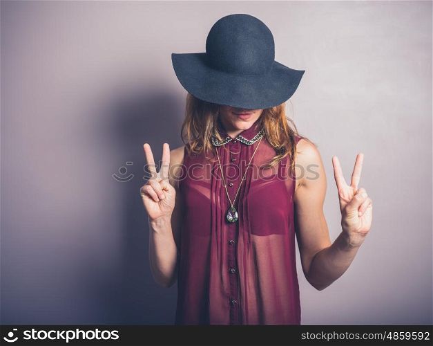 A sexy and fashionable lady wearing a hat and a see through shirt is showing the v sign