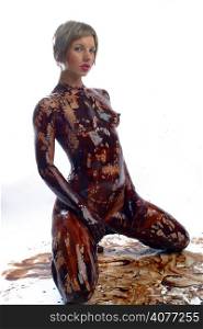 A sexy model covered from head to toe in chocolate poses in the studio.