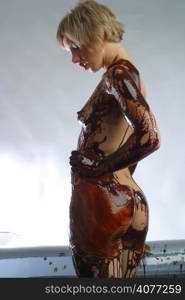 A sexy model covered from head to toe in chocolate poses in the studio.