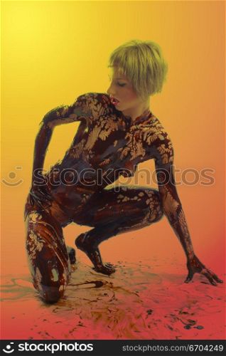 A sexy model covered from head to toe in chocolate poses in the studio.